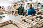 Portrait of a team of two mixed race male and female carpenters in a large woodworking factory.