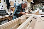 Senior Caucasian  carpenter sanding a wooden cabinet part in a large woodworking shop.