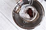 A metal bowl with ingredients and a sieve with cocoa powder.