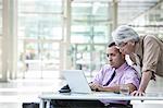 An Asian businessman and Caucasian businessman working on laptop computer in the lobby of a convention centre.