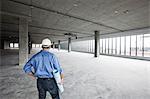 A Caucasian male architect standing looking out over a new raw business space.