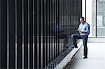 A Caucasian male architect standing by a wall of windows, using a digital tablet.