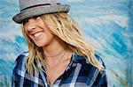 Portrait of smiling woman with long blond hair wearing blue checked shirt and grey Trilby hat.