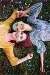 Two young women covered in coloured chalk powder lying on grass at Holi Festival, overhead portrait