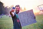 Young man taking selfie holding free hugs sign at Holi Festival