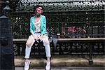 Young woman with pink hair and quirky style sitting on bench, London, UK