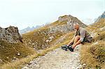 Hiker tying laces on dirt track, Canazei, Trentino-Alto Adige, Italy