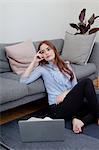 Woman sitting on floor against sofa using laptop