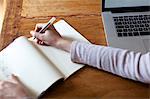 Woman writing notes into notepad from laptop