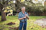 Smiling senior man raking autumn leaves in backyard