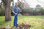 Senior man raking autumn leaves in backyard