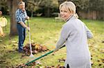 Portrait happy mature woman raking autumn leaves in backyard