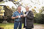 Smiling mature couple drinking coffee and raking autumn leaves in backyard