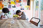 Focused brother and sister coloring at dining table