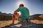 Young male climber sitting on top of rock formation, Tuolumne Meadows, upper part of the Yosemite National Park, California, USA