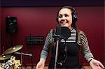 Confident teenage girl recording music, singing in sound booth