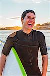 Laughing male surfer with surfboard on beach