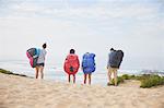 Paragliders carrying parachute backpacks on ocean beach