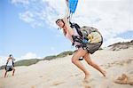 Female paraglider running, taking off on beach