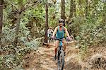 Carefree woman mountain biking on trail in woods