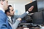 Businessmen trading stocks online. Stock brokers looking at graphs, indexes and numbers on multiple computer screens. Colleagues in discussion in traders office. Business success concept.