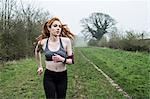 Young woman with long red hair wearing sports kit, exercising outdoors.