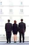 Rear view of group of three business people looking out the window of a conference centre lobby.