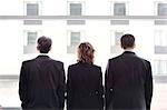 Rear view of group of three business people looking out the window of a conference centre lobby.