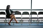 Caucasian businesswoman sitting in a row of chairs against a window in a conference centre lobby.