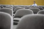 Single businessman sitting in a room full of chairs prior to a conference centre meeting.