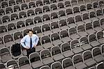 View from above looking down on a businessman standing alone in a room full of chairs prior to meeting in a conference centre.