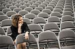 A businesswoman sitting alone in a room full of chairs prior to a meeting in a conference centre.