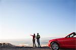 A young Caucasian couple admires the view at a rest stop in Eastern Washington, USA while on a road trip with their convertible sports car.