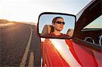 A young Caucasian woman reflected in side mirror of a convertible sports car on the highway.