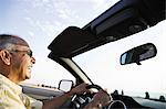 An Hispanic senior man laughing and driving his convertible sports car.