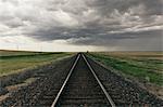 Train tracks through prairie and farmland, storm clouds in distance