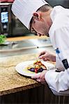 A Caucasian male chef putting the finishing touches on a plate of fish in a commercial kitchen.