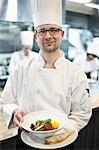 A Caucasian male chef presenting a finished plate of fish in a commercial kitchen