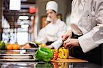 A closeup of the hands of a chef cutting vegetables in a commercial kitchen.