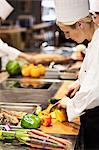 A Caucasian female chef works cutting vegetables in a commercial kitchen,