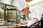 A Caucasian female chef putting the finishing touches on a plate of fish in a commercial kitchen.