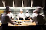 A blurred view of a crew of  chefs working around a commercial kitchen.