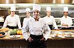 A portrait of a black female chef and her team of chefs in the background of a commercial kitchen,