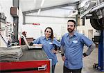 A portrait of two Caucasian male and female mechanics in an antique car repair shop.