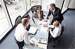 A mixed race group of male and female business people in a meeting at a conference table next to a large window in a convention centre.