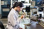 A Caucasian female technician using a microscope to examine a part in a technical research and development site.