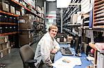 A portrait of a Caucasian male technician sitting at his desk in a parts department in a technical research and development site.