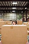 A Caucasian female warehouse worker behind a cardboard box in a distribution warehouse.