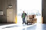 Male warehouse worker standing next to a manual pallet jack and cardboard boxes in a distribution warehouse.