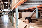 A black female worker hiding inside a cardboard box in a distribution warehouse.
